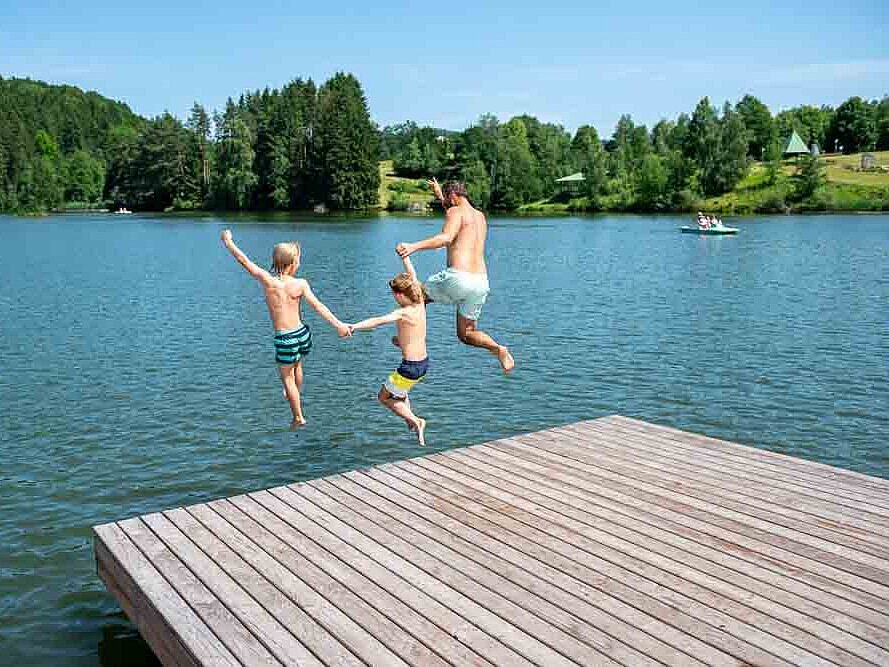 Ein Vater und zwei Kinder springen vom Badesteg in den See